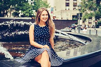 Eine Frau in einem blauen Sommerkleid sitzt auf einem Brunnen-Rand.