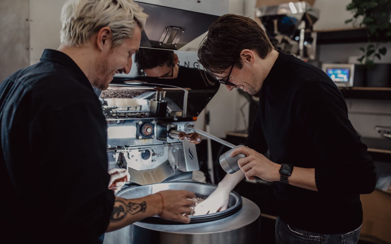 Zwei Mitarbeiter der Rösterei sometime rühren Kaffeebohnen in einer Trommel um