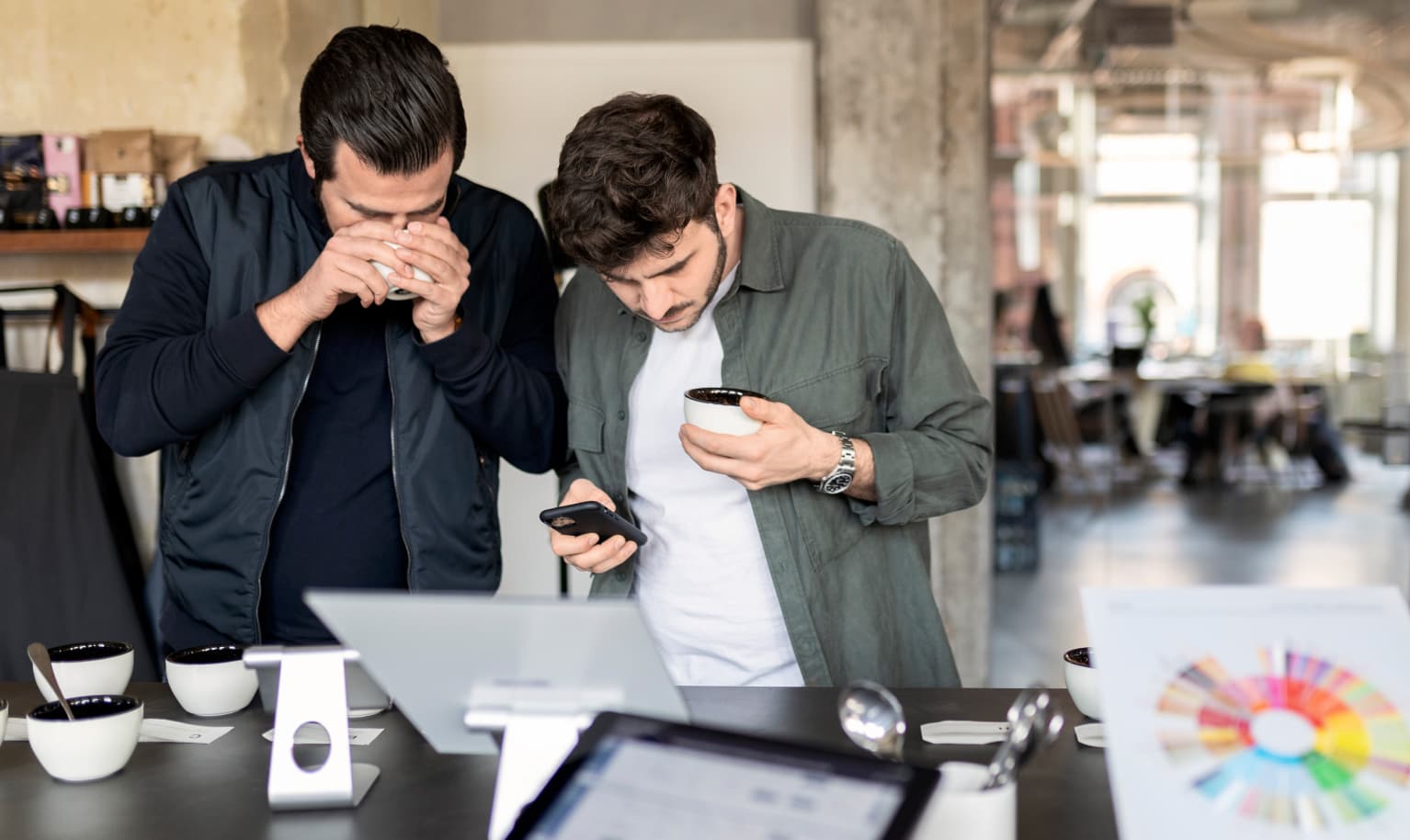 Zwei Männer stehen an einem Cupping Tisch und verkosten Specialty Coffee nach dem SCA Protokoll.