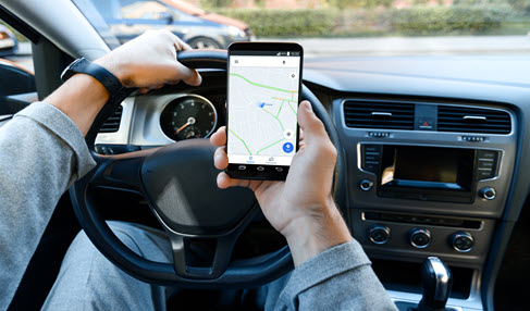 Mann, der im Auto auf seinem Smartphone eine Onlinekarte geöffnet hat.