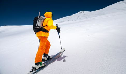 Die richtige Skihose: Ein Mann geht in einer gelben Skihose einen Schneebedeckten Berg hoch.