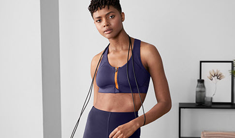 Stay on track: Eine junge Frau macht zu Hause ein Workout in einem dunkelblauen Sportoutfit.