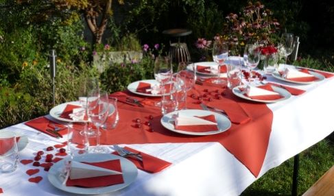 Eine feierlich dekorierte Tafel, mit einer weißer Leinentischdecke. Der Tisch ist mit schlichten Tellern, Besteck und roten Herzen gedeckt.