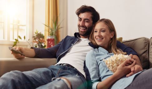 Pärchen sitzt mit Popcorn auf dem Sofa und sieht fern.