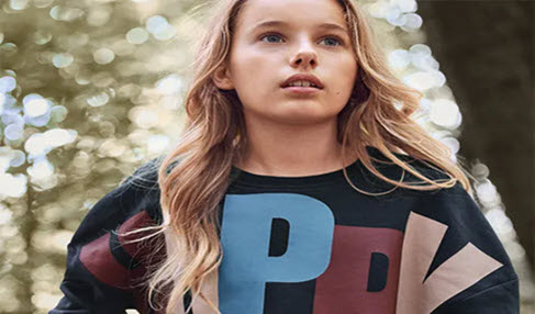 Ein Mädchen trägt einen Sweater mit dem großen Aufdruck Happy in bunten Farben.