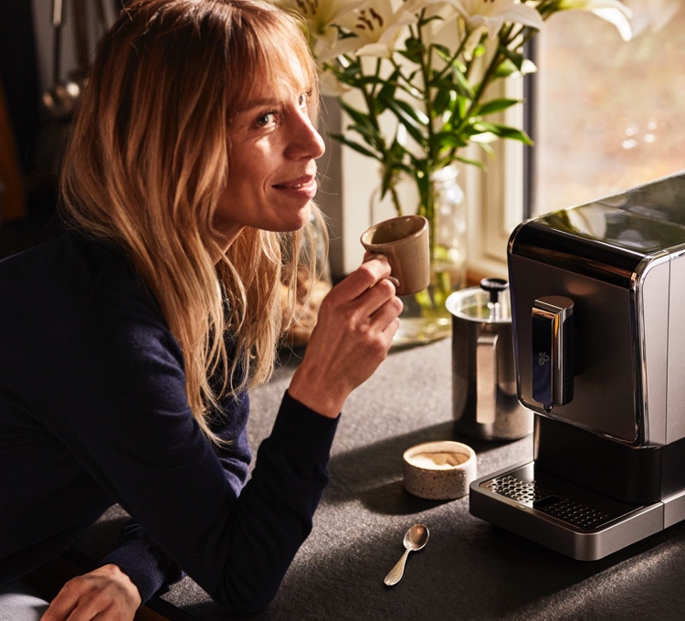 Stimmungsvolles Bild einer in die Kamera lachenden Frau, die sich über ihren Kaffee aus dem Esperto Caffè freut.
