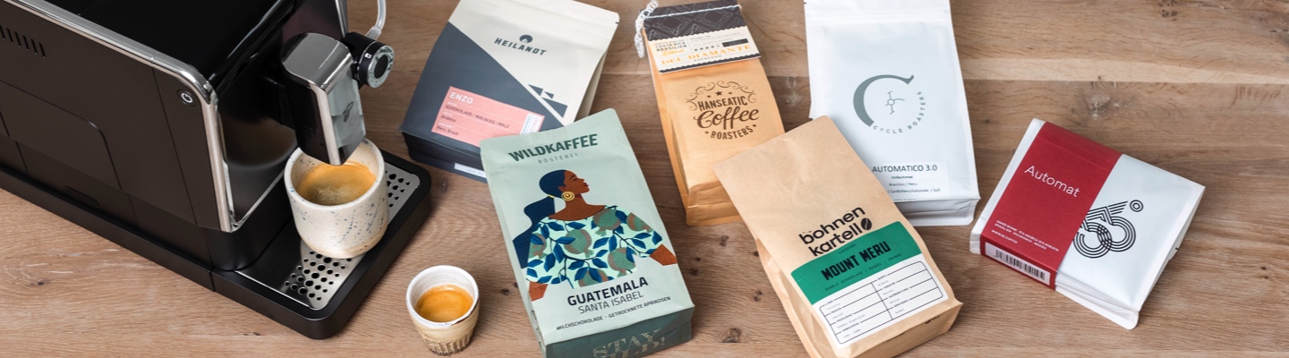 Eine große Auswahl an Specialty Coffee liegt auf Tisch neben einem Vollautomaten.