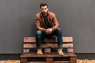 Ein Mann mit Lederjacke und Jeans sitzt draußen.