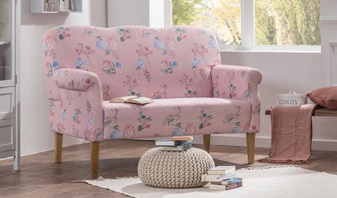 Die perfekte Größe: Ein rosa Küchensofa mit floralem Muster steht an einem Fenster. Davor ein kleiner Couchtisch in hellrosa.