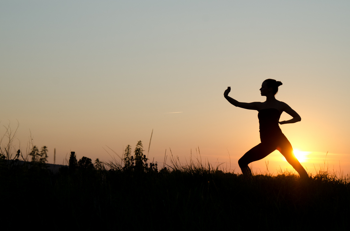 Frau beim Tai Chi Chuan bei Sonnenuntergang.