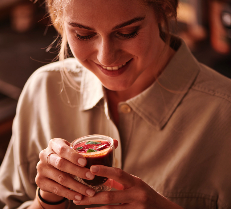 Eine Frau trinkt ein Kaffee-Milchgetränk aus einem Latte Macchiato Glas und lächelt dabei
