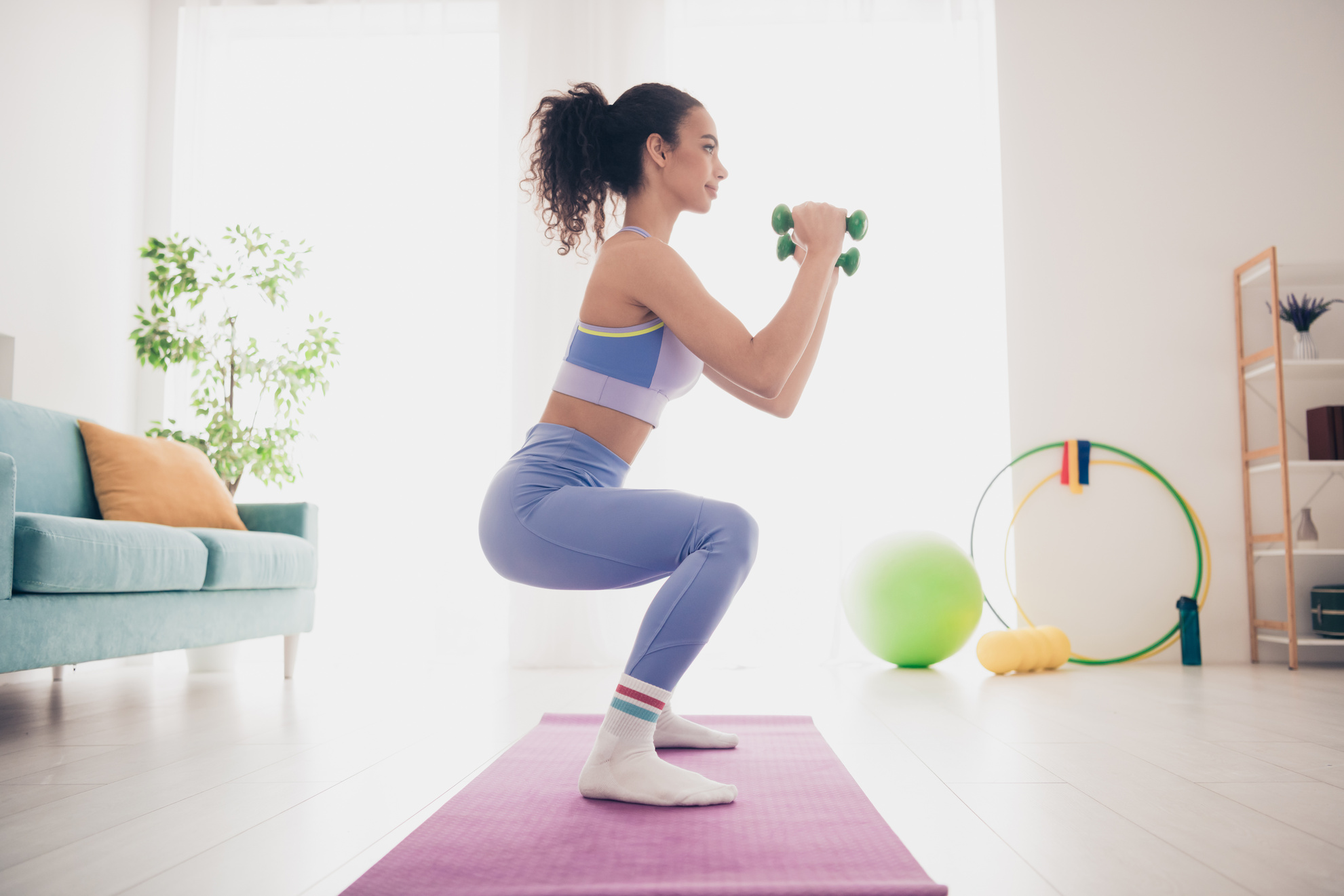 Junge Frau, die zu Hause mit Hanteln trainiert und sich in einem stilvollen und hellen Wohnzimmer der Fitness widmet.