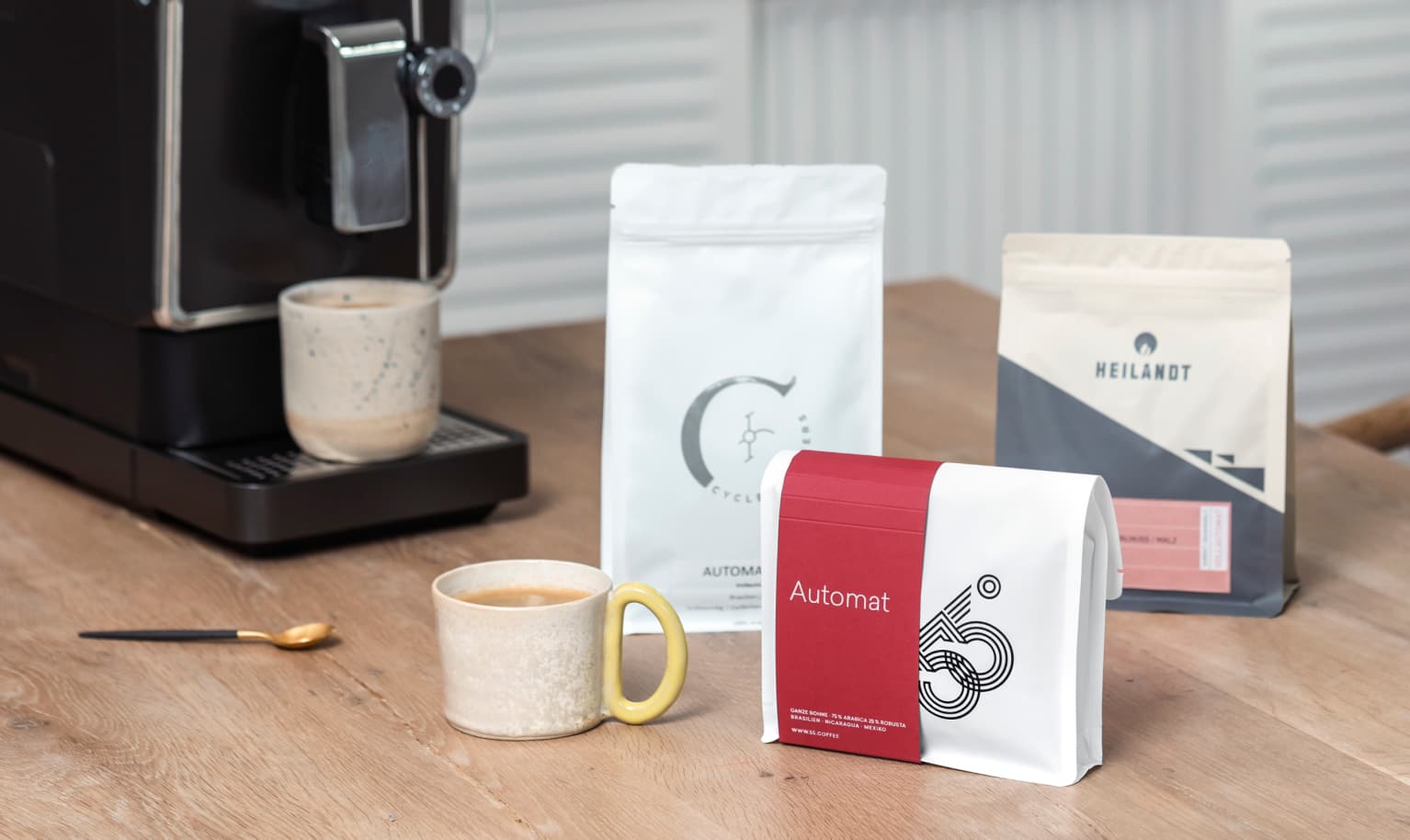 Ein Probierpaket aus drei 1-kg-Packungen Specialty Coffee steht neben einem schwarzem Vollautomaten auf einem Tisch.