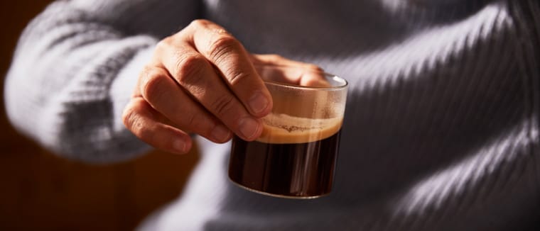 Eine männliche Hand hält ein Glas mit Kaffee.