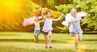 3 Kinder in Sommerkleidung rennen im Garten