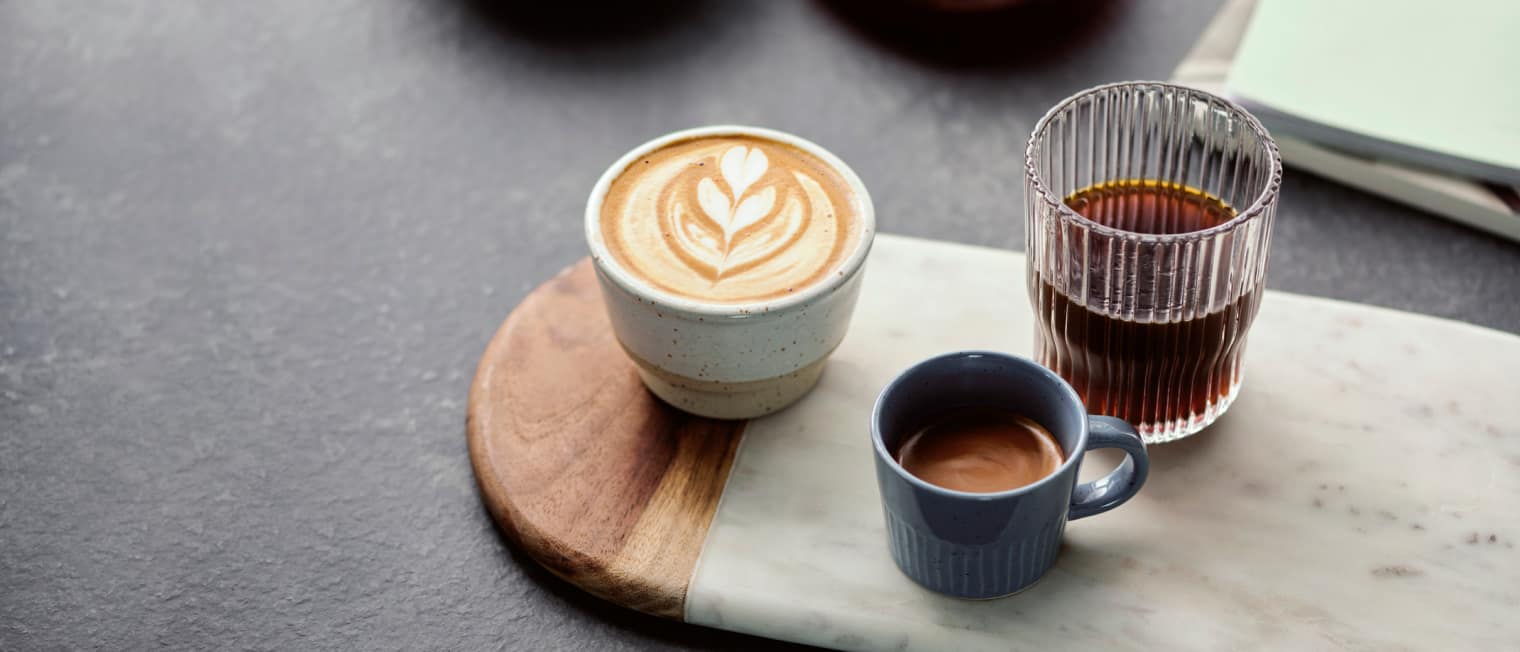 Verschiedene Kaffeegetränke stehen stilvoll auf neben eines Holzbretts in der Küche.