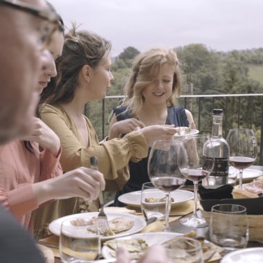 Freunde sitzen auf Terasse, essen und trinken Wein.