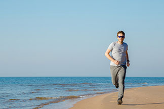 Ein junger Mann läuft in einer klassischen, grauen Jogginghose am Strand entlang.