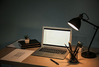 Der richtige Platz für das Licht: Eine schwarze Bürolampe steht auf einem Holzschreibtisch neben einem Laptop.