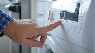 Herrenweste richtig waschen: Nahaufnahme einer Männerhand beim Einschalten einer Waschmaschine.
