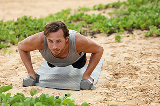 Ein durchtrainierter, junger Mann in einem ärmellosen Sportshirt macht seine Fitnessübungen an einem Strand