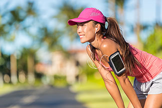 Eine junge Frau beim Joggen mit Cap und Musicplayer bei sonnigem, sommerlichen Wetter.