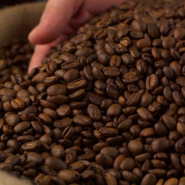 Hand fährt durch geröstete Kaffeebohnen.
