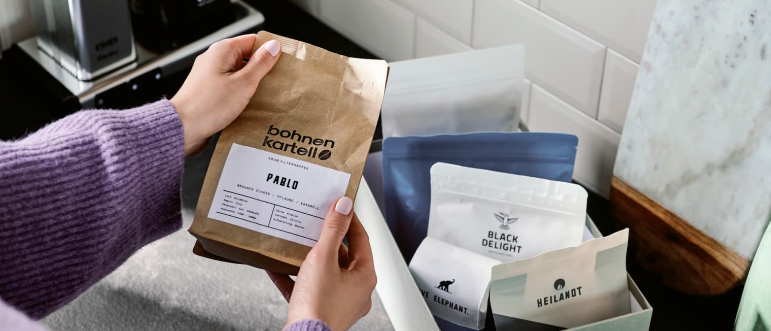 Jemand nimmt eine Packung Kaffee aus einem Karton mit verschiedenen Packungen Kaffee