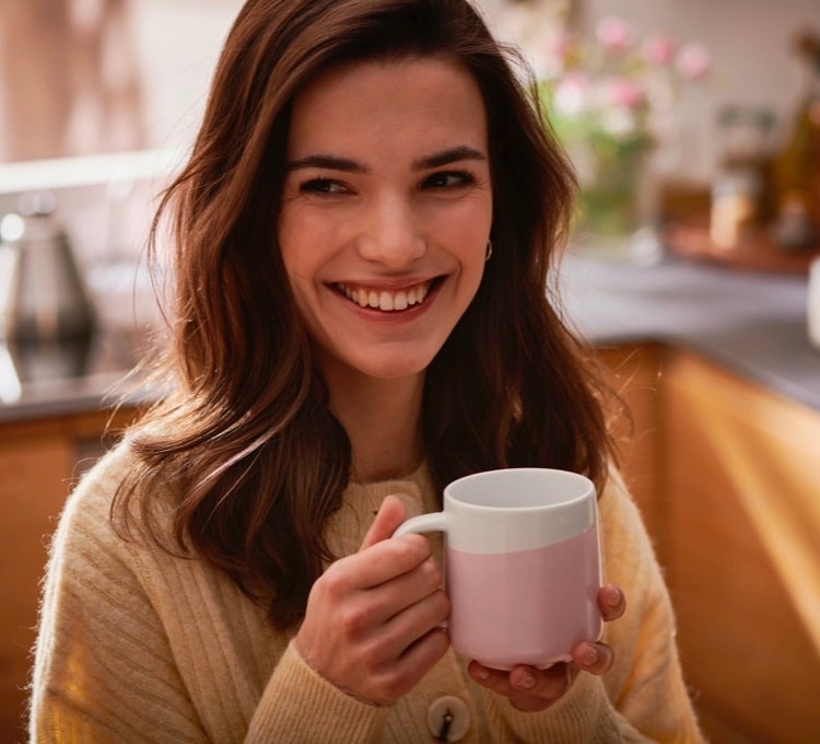 Eine Frau trinkt ihren Kaffee aus einem rosa Kaffeebecher der Porzellanserie.