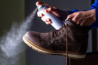 Nahaufnahme eines Leder-Herrenstiefels, der gerade mit einem Spray imprägniert wird.