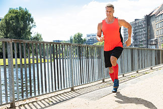 Ein Läufer mit orangenen Sportsocken joggt auf einer Brücke neben einem Fluss.
