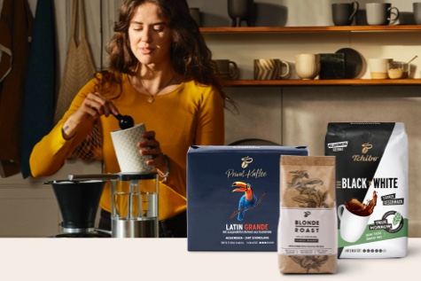 Eine Frau löffelt gemahlenen Filterkaffee aus einer Dose, daneben sind der Latin Grande, Black and White und Blonde Roast präsentiert.