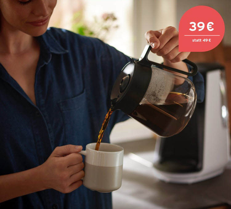 Eine Frau trinkt genüsslich ihren Kaffee aus einer Filterkaffeemaschine, die im Hintergrund zusehen ist.