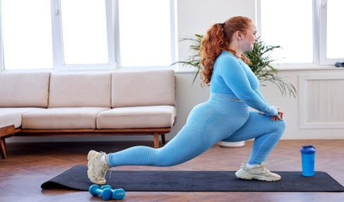 Das perfekte Set: Eine junge Dame macht zu Hause Sport und trägt dafür ein blaues Sportshirt und eine blaue Sporthose.