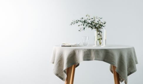 In der Mitte eines Raumes steht ein runder Tisch auf dem eine graue Tischdecke liegt. Auf dem Tisch steht Dekoration.