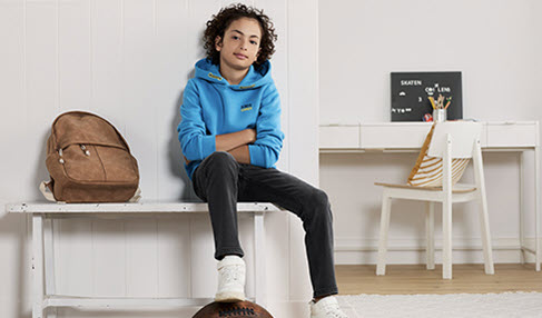Weniger ist mehr: Ein Junge sitzt auf einer Bank in einem schlichten blauen Hoodie.