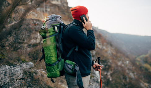 Mann mit Rucksack und Wanderstöcken in den Bergen, während er mit einem Handy telefoniert.