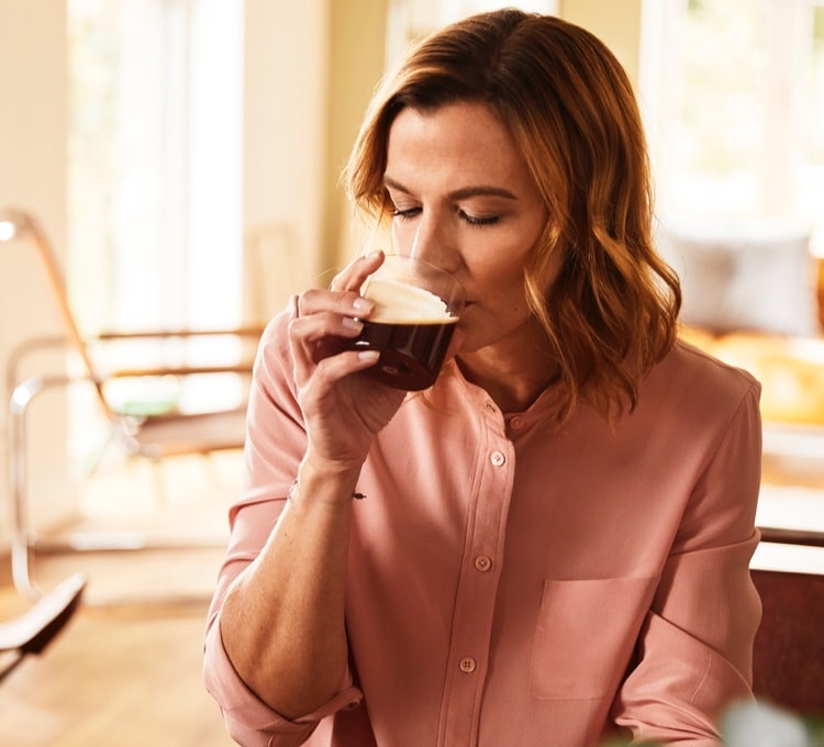 Rothaarige Frau nippt an einem Glas Espresso Kaffee, hier finden Sie die besten Kaffees für Ihre Siebträgermaschine.