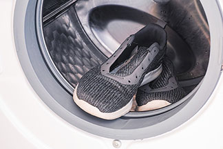 Halbschuhe für Herren richtig pflegen: Graue Herrensneaker mit entfernten Schnürsenkeln in einer Waschmaschine.