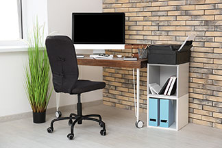 Wichtige Büroausstattung: Ein schwarzer Bürostuhl ohne Armlehnen steht vor einem Holzschreibtisch auf dem ein Monitor steht.