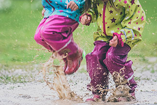 Kinder spielen mit Regenkleidung in Pfütze