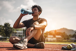 Sneackersocken für den Sport: Ein junger Mann sitzt auf einem Sportplatz und trinkt aus einer Wasserflasche.