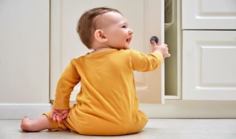 Ein Baby öffnet die Schranktür seines Kinderkleiderschrankes und lacht dabei.