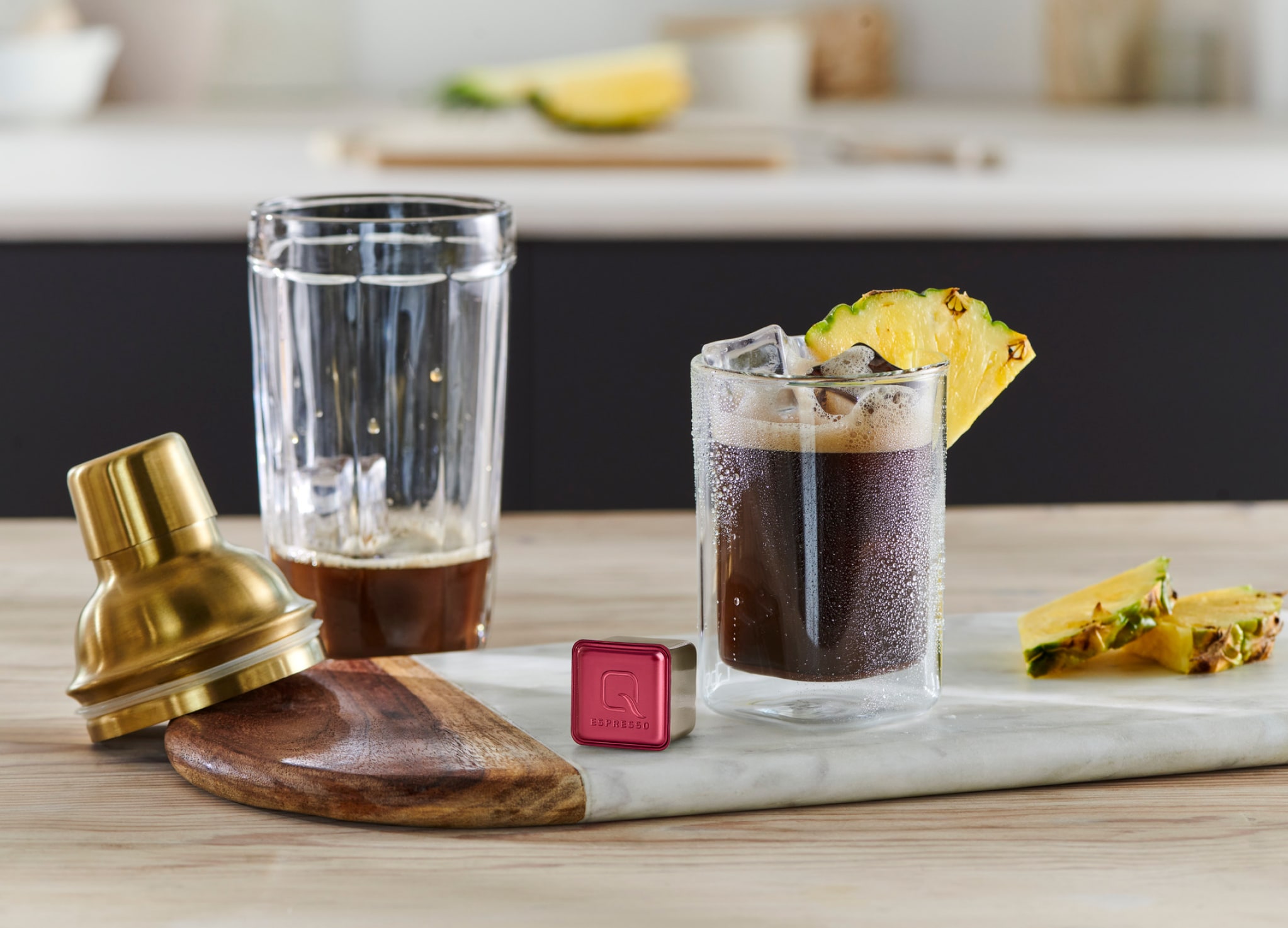 Kaffee steht mit Ananasscheibe, Qbo-Kapsel und Cocktail-Zubehör auf Tresen