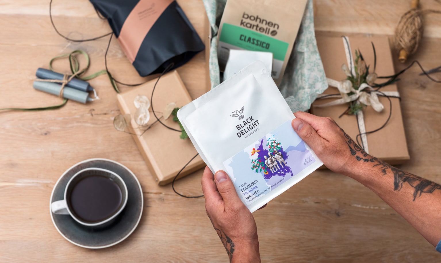 Jemand hält eine Packung Kaffee in den Händen während auf dem Tisch darunter zwei weitere Packungen und Geschenkpapier liegen