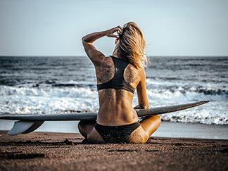 Frau sitzt im Bikini am Strand
