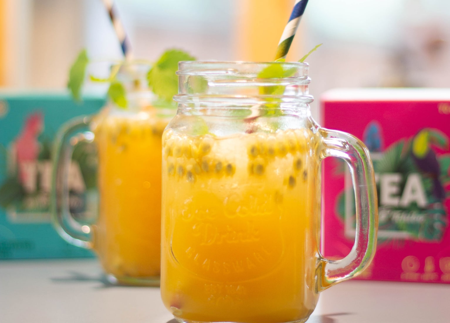 großes Marmeladenglas mit Passionsfrucht, Minze und Strohhalm mit Tchibo-Tee im Hintergrund
