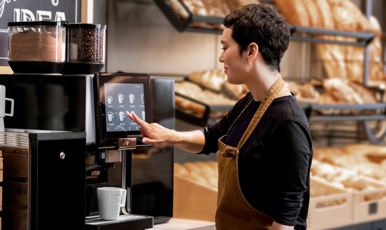Frau bedient Kaffeevollautomaten in einer Bäckerei