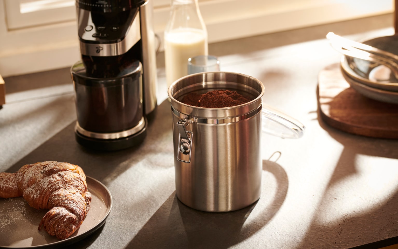 Croissant links, Kaffeemühle und Kaffeedose mit Kaffee