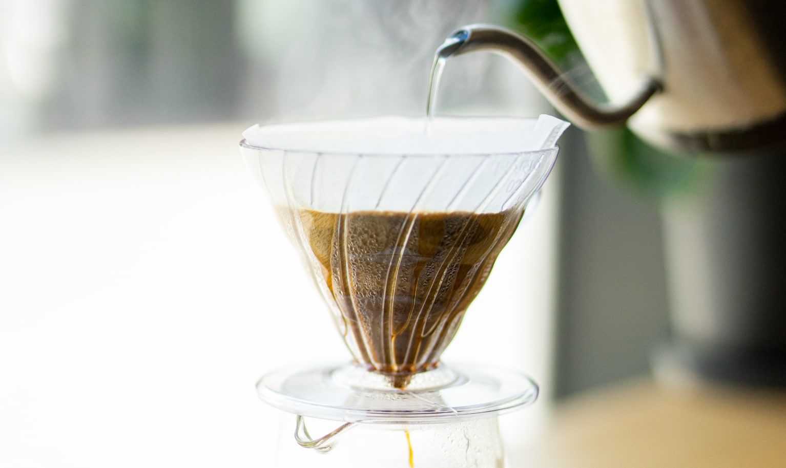 Jemand gießt heißes Wasser in einen Kaffeefilter während der fertige Kaffee unten in die Glaskaraffe läuft.
